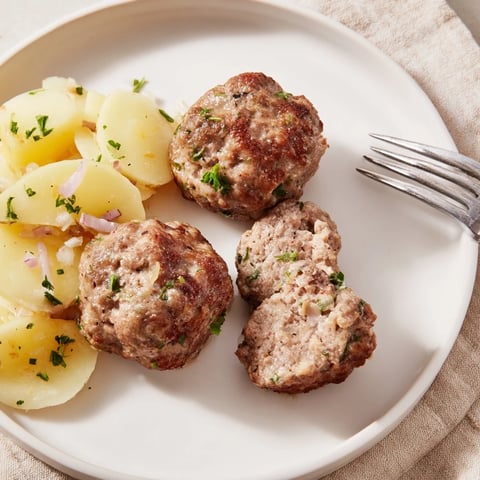 Saftige, goldbraune Fleischbällchen gereicht mit cremigem Kartoffelsalat für gemütliche Familienessen.  